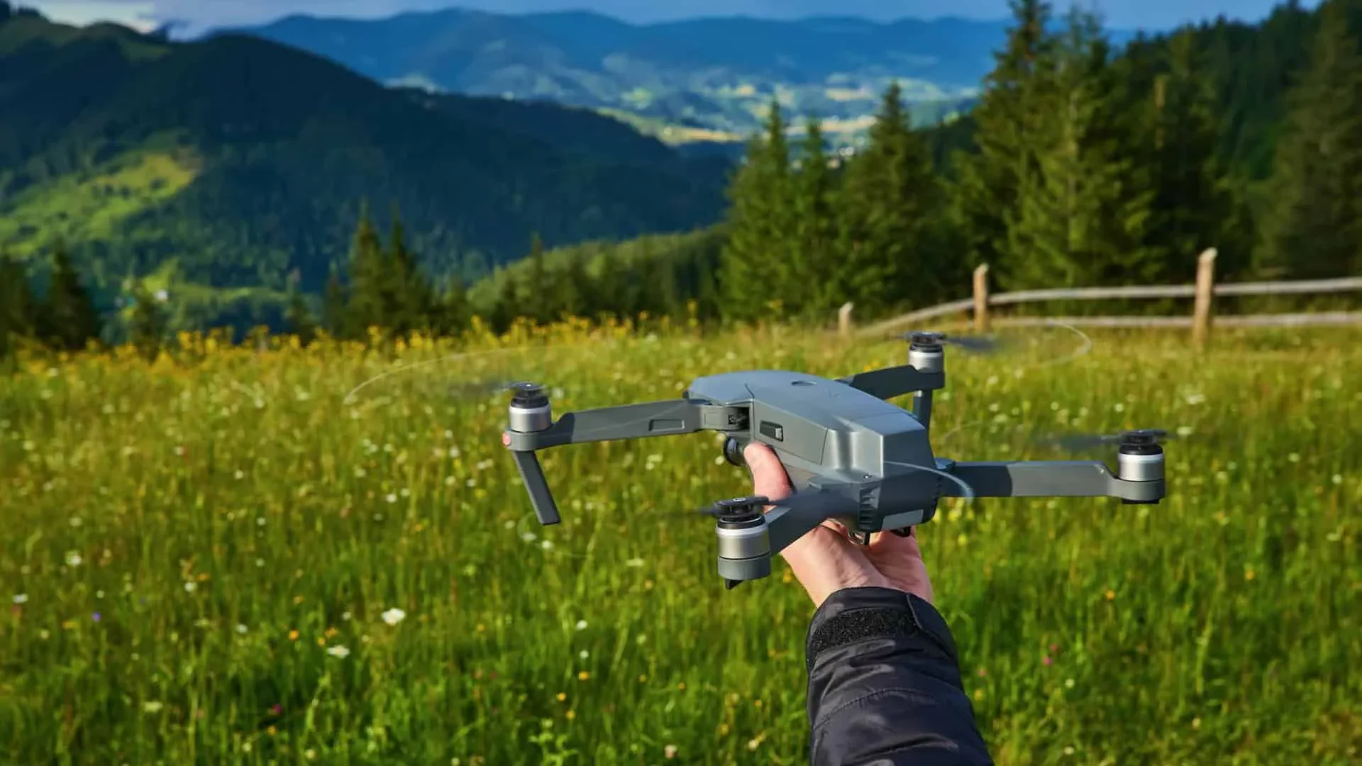 Drone flying over lush mountain meadow with green grass and trees.